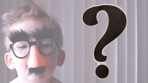 A child wearing Groucho Marx glasses; a question mark to the side