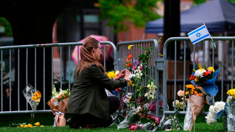 A woman places a bouquet of flowers along a guardrail where other flowers have been left.