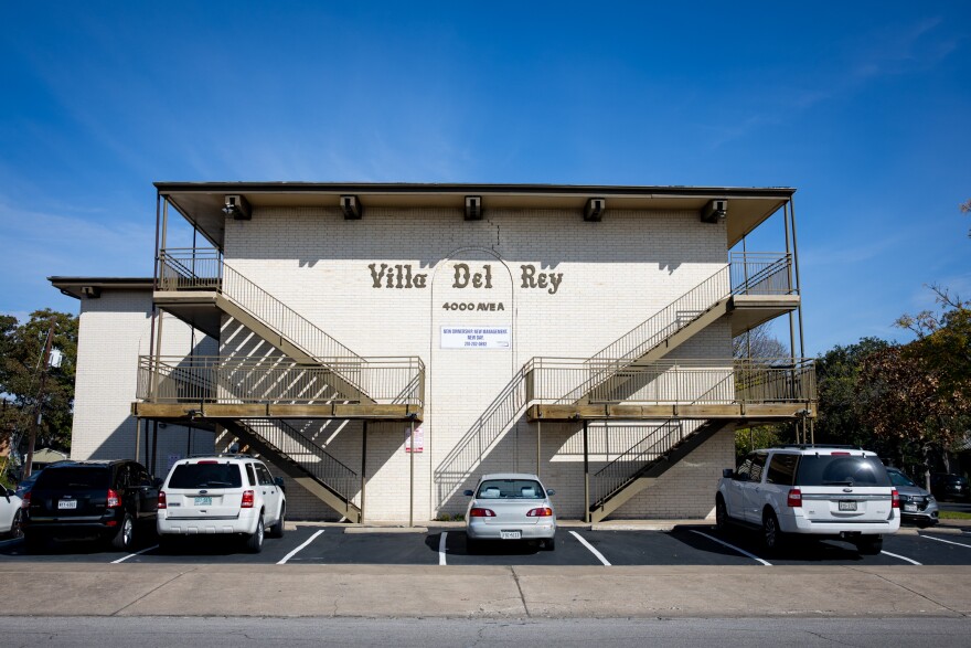 The facade of the Villa Del Rey apartment complex wiht cars parked in a parking lot