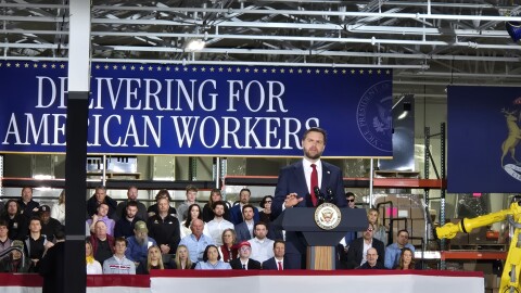 JD Vance speaks at a lectern in front of a blue banner that reads "DELIVERING FOR AMERICAN WORKERS."
