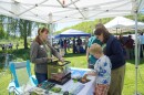 Alissa Pendorf (left) shows off an Eastern Gray Treefrog to a family at Frog Fest. The frog is on top of the branch on the lefthand side of the box. There's another frog in the box hiding underneath the foliage. 