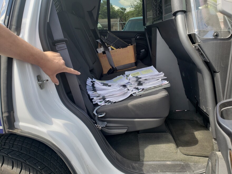 Deputy Constable Alex Chavez points to court papers filling the backseat of his patrol unit. The paperwork is from the Attorney Generals’ Office and is waiting to be served.