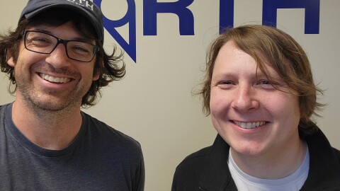 Close-up of two people smiling at the camera with "The North" written in blue on a white wall behind