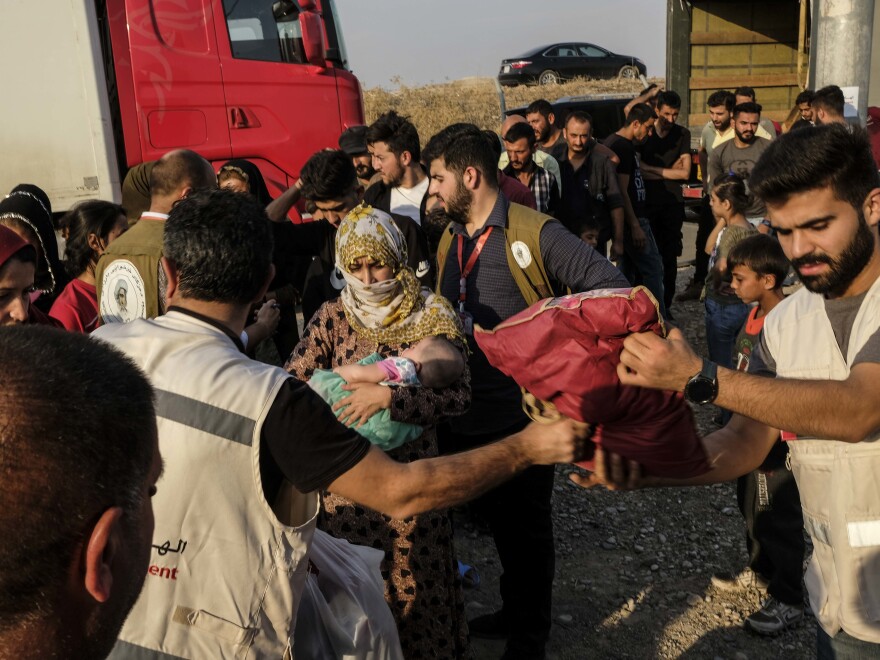 Syrians fleeing the Turkish incursion in northeastern Syria receive bedding materials as they arrive at a camp in Dohuk, Iraq, on Thursday.
