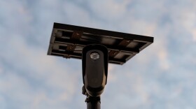 A camera on a tall pole with a solar panel on top.