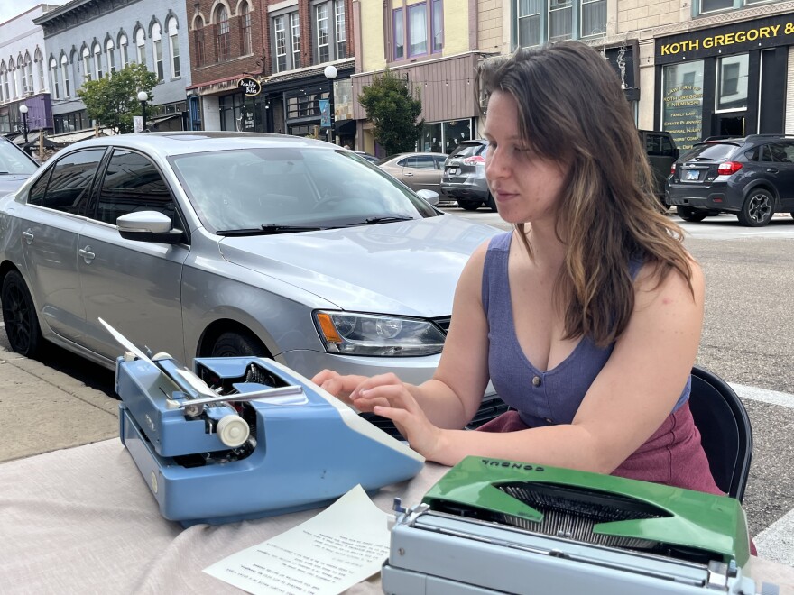 Woman typing on a powder blue typewriter with a green typewriter to her left.