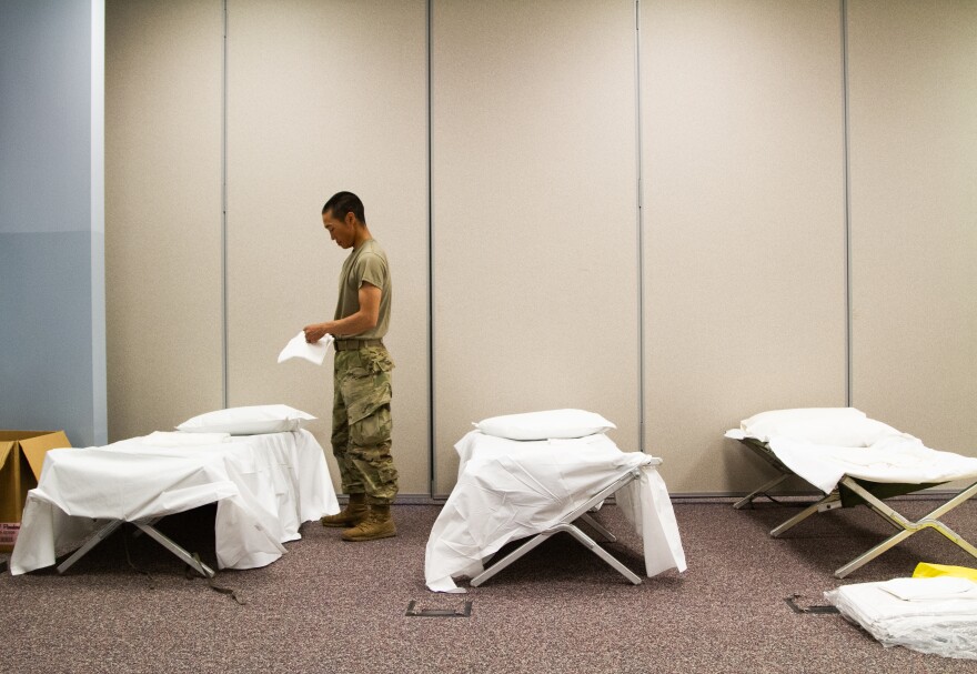 Army National Guardsmen pull creased bedding out of plastic packaging.