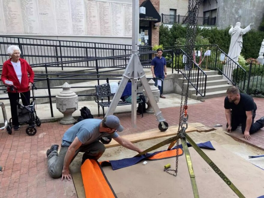 Workers install the sculpture outside of St. Leonard's in the North End. Nancy Schön, left, looks on eagerly.
