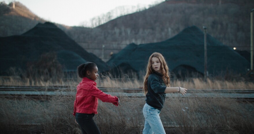 Two girls dance in front of mounds of coal.