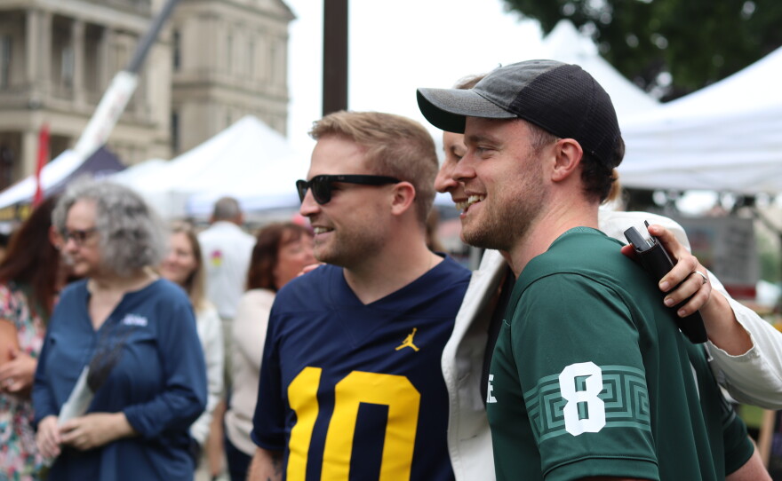 Photos of Josh and Jace, two young British men, taking photos with fans and mascots. The two are wearing a blue University of Michigan and a green Michigan State University jersey respectively.
