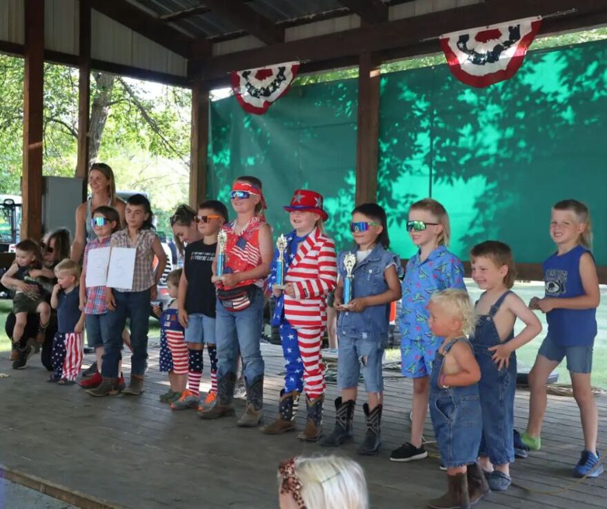 All thirteen contestants line up showcasing their trophies and mullet hairstyles | MPR News