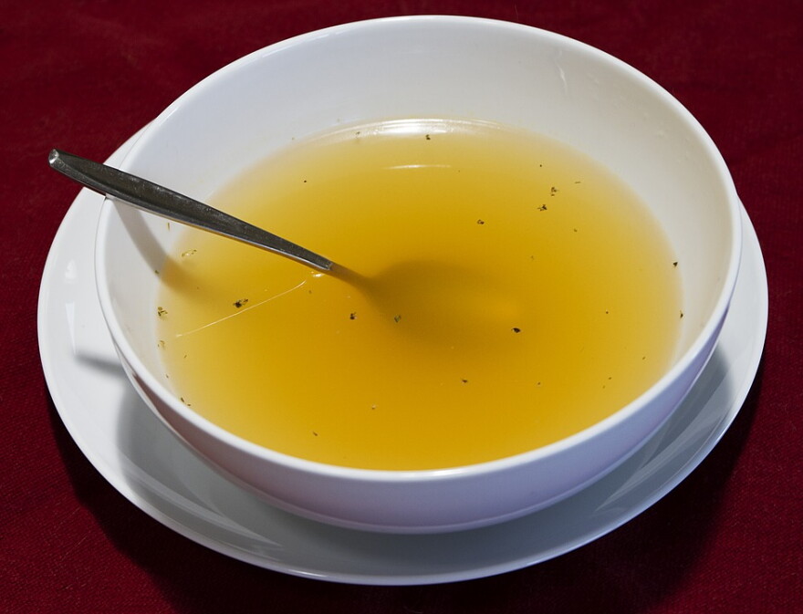 A white bowl of broth on a plate with a spoon
