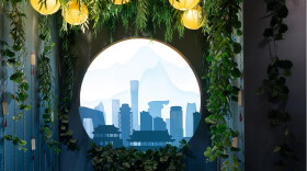A round window framed in vines looks out onto a blue cityscape