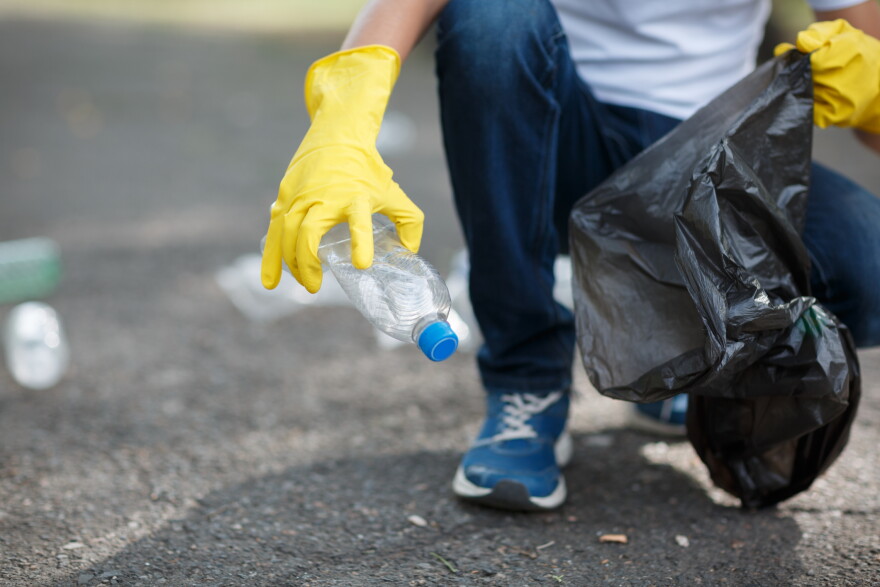 Hands in yellow gloves picking up empty of bottle plastic into bin bag on asphalt, volunteer and purity concept. Enviromental protection.