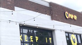 Windows on a storefront feature a yellow chicken logo and lettering spelling out "Keep It Pop Up," along with a Pop-Up restaurant sign sign on a brown brick background. 