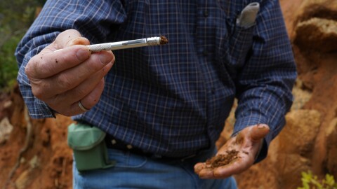 A man with a magnetic pen covered in red soil, more red soil in the background. 