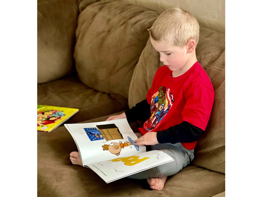 Bjorn Alder, a Lewiston recipient of the Dolly Parton Imagination library, reads cross-legged on a couch.