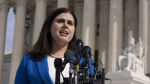 A woman in a blue jacket speaks in front of the U.S. Supreme Court building.