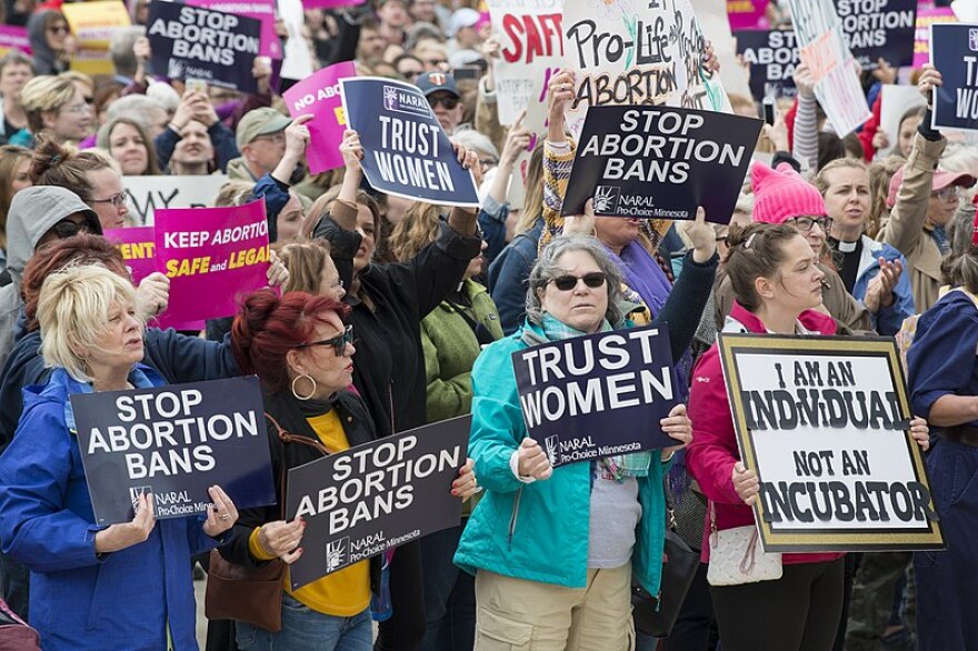 a crowd of people hold signs reading "Stop abortion bans" and "trust women"