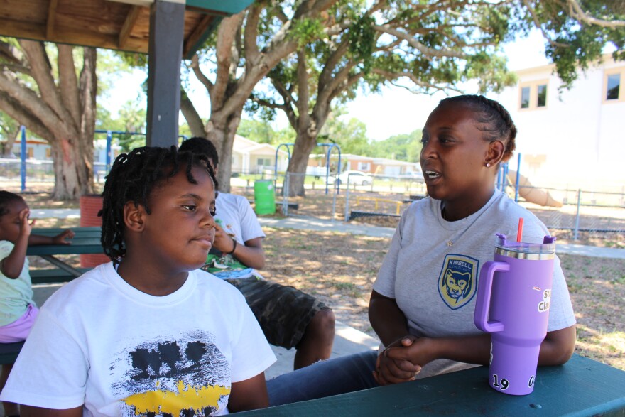 A mother and her daughter sit at a park picnic table