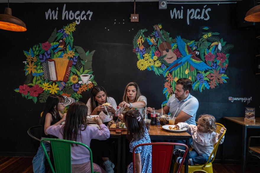 DO NOT USE / New York Times — Customers at Los Chamos, a Venezuelan restaurant chain known for its arepas, in Medellin, Colombia, where a mural shows Colombia on the left, with the words “my home,” and Venezuela on the right, with the words “my country,” Sept. 29, 2024. Colombia and Venezuela claim the cornbread as their own, but where does it really come from? And who makes it better?