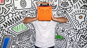 An orange boom box is held in front of doodled mural