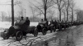 Black-and-white photograph of the Cadillac Motor Company Road Testing Department, showing men in early automobiles lined up on a snowy, wet road in 1912.