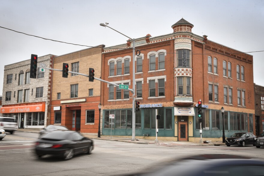 Blurring cars move past a three-story, brick building located at the intersection of 31st and Main Streets in Kansas City, Missouri.