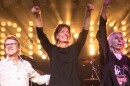 Three old men in stage with lights behind them. Two of them have their hands up 