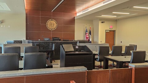 An empty courtroom with chairs and tables in front of a judge’s bench.