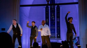 Four actors appear on stage with blue lighting behind them. 