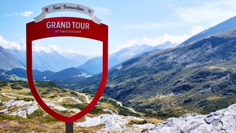 A view of San Bernardino Pass, a destination of the the European Grand Tour, Schweiz. Snow covered mountains and rolling valleys against a blue sky with wispy clouds.