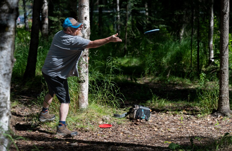 A man in a blue baseball cap and shorts throws a frisbee gold disc.