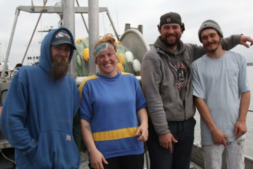 Four people stand on the deck of a boat, posing for a photo.