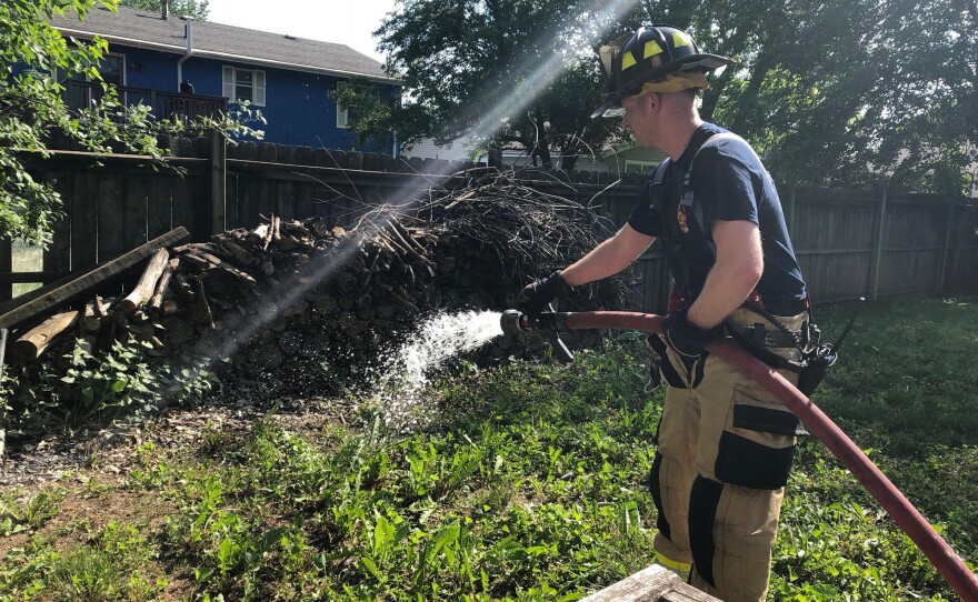 Firefighter sprays water on a wood pile.