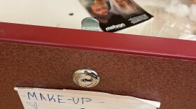 In the foreground, the front of an open drawer with an index card attached that says "make-up stuff" in handwritten letters. Inside the drawer, out of focus, is a label with pictures of people in gray hair and beards that says "Aging" at the top.