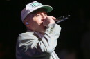 Man with a white baseball cap and brown sportcoat singing into a microphone