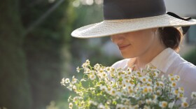a woman wears a sun hat that covers her eyes while she holds a bouquet of daisies 