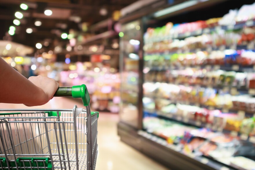 A woman holds a supermarket shopping cart in a grocery store.