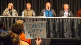 One attendee holds up a sign that says "conserve water now" in front of the panel of Google representatives on Thursday. One representative outlined Google's planned requests for further wetland mitigation credits as well as a plan to relocate Adams Ditch on the property.