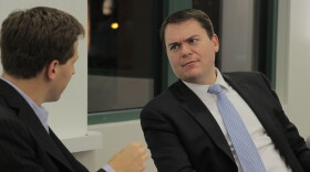 Two white men in suits face each other seated, with the man at left facing away from camera. At right Carl DeMaio frowns at the other man, leaning back. 
