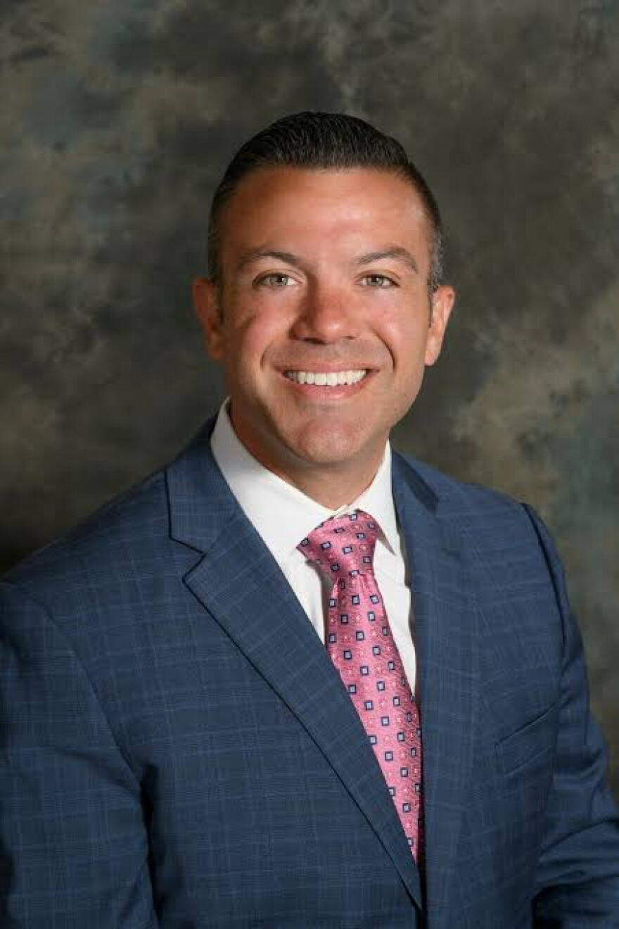 A man in a suit and red tie smiles for the camera.