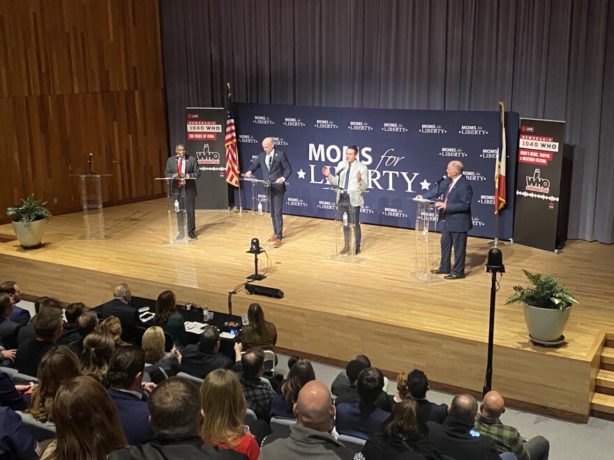 four men stand at podiums on a stage