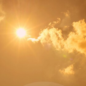 Bright sun flaring in sky with some clouds and yellowish cast to whole photo