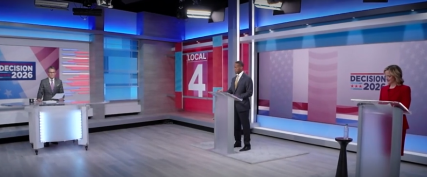 Gubernatorial candidates Jocelyn Benson, in a bright red suit, and John James, in a gray suit, debate in a TV studio.