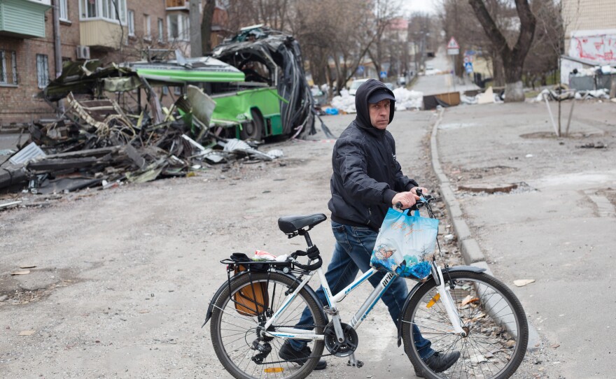 A man walks his bicycle in Kyiv on March 28, near a tram that was destroyed by a rocket strike weeks earlier. Russia said on Tuesday that it will reduce its military activity around Kyiv and other parts of northern Ukraine.