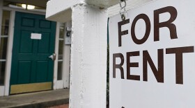 A white for rent sign hands in front of a home with a dark blue door.