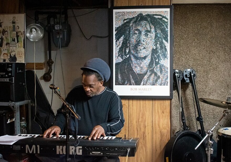 A poster of reggae icon Bob Marley hangs on the wall as Ronnie "Skill" Gordon rehearses with Ignite Reggae Band.