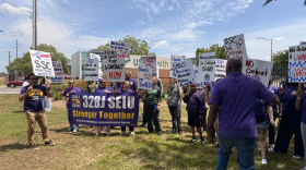Un grupo de manifestantes, vistiendo camisetas moradas y sosteniendo carteles tanto en inglés como en español, pidiendo salarios más justos.