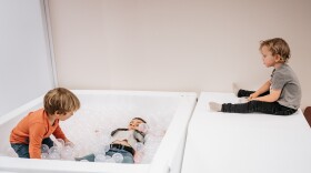 Three children are playing with a white ball pit, filled with clear plastic balls. 
